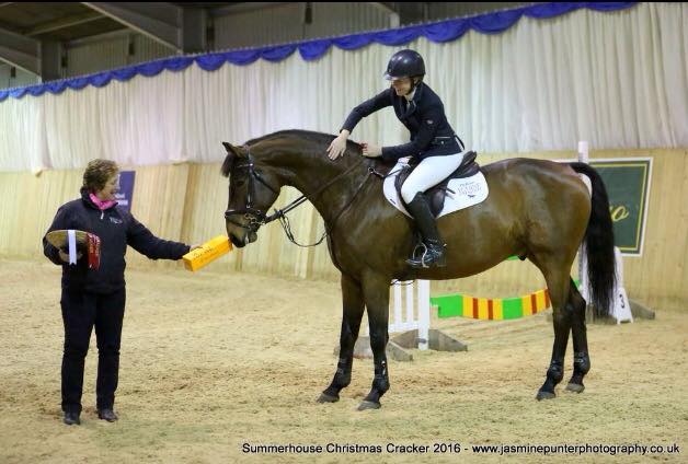 Bay horse and rider collecting a rosette at an indoor prizegiving