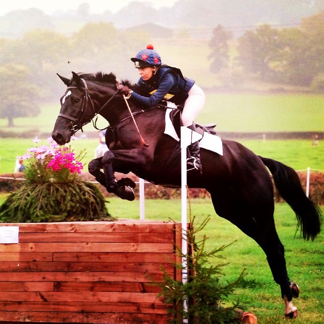 Lucy Morgan jumping a black sport horse over a cross-country log fence